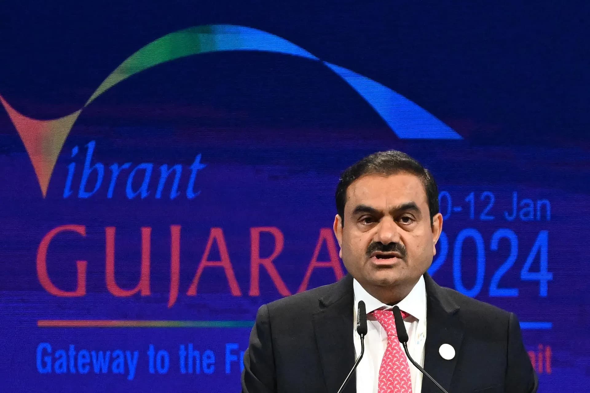 Gautam Adani speaking at a business summit in front of a Vibrant Gujarat backdrop