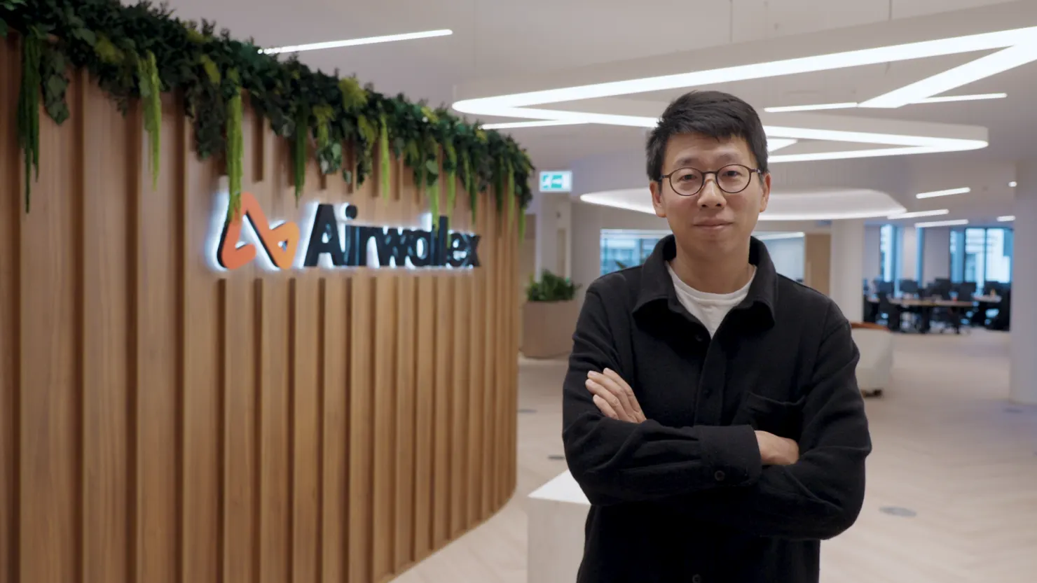 Jack Zhang, co founder and chief executive of Airwallex, standing in the company's office beside its logo