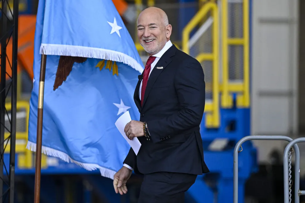 Jeff Bezos smiling as he walks past a flag at an event