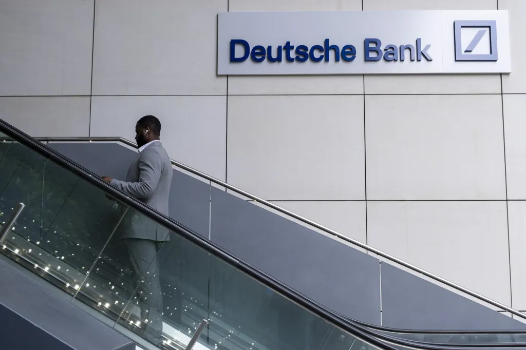 A commuter rides an escalator past a large Deutsche Bank sign