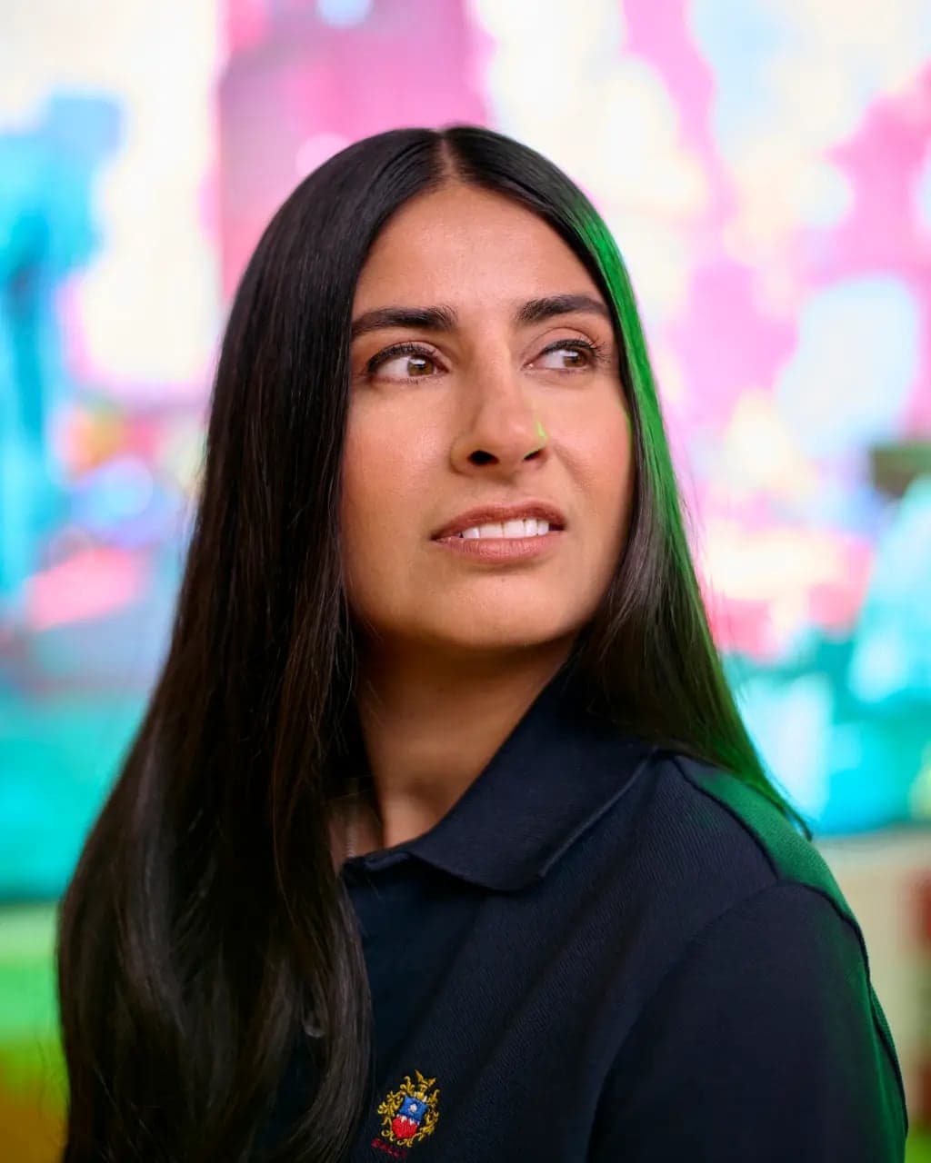 Asha Sharma looking upward in a dark polo shirt against a colorful blurred background